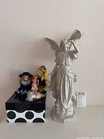 Front view of all items together: angel figurine, three dolls on polka-dot box