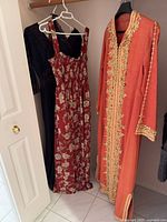 Three dresses hanging: black lace, red floral sundress, orange embroidered kaftan