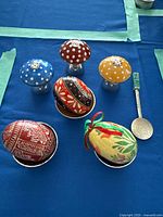 Three sterling toadstool shakers, three enamel interior egg cups with painted eggs, Mexican spoon