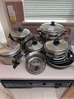 Overall group of nested stainless steel pots, pans and steamer inserts on counter