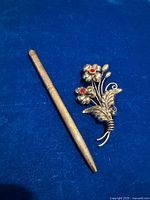 Brooch and pen side by side on blue cloth