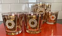 Front view of lowball and highball tumblers showing gold starburst and white wreath design