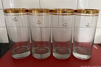 Front view of four tall glasses showing Paşabahçe logo and gold bands