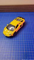 Top view of yellow Lamborghini Aventador die-cast model on blue grid mat