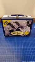 Front view of metal lunch box showing Three Stooges image and 'DVDs Inside' text