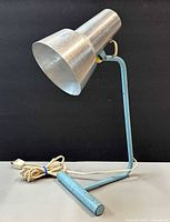 Left-side view of blue metal desk lamp showing aluminum shade, frame, and cord