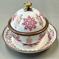 Domed lidded bowl seated on matching plate showing pattern and brass finial