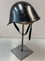 Left front view of Dutch M34 black steel helmet on stand, showing overall shape and finish