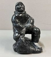 Front view of seated Inuit soapstone figure holding bundle