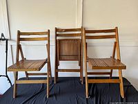 Three walnut wooden folding chairs, slatted seats and backs, folded and unfolded positions visible
