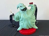 Front view of glow-in-the-dark Oogie Boogie popcorn bucket on red base with attached black Disney lanyard
