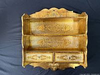 front view of gilt wooden wall shelf showing two shelves and drawers