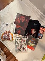 Full lot overview showing poster, two t-shirts, notebook, pencil holder box, tumbler