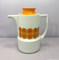 Front view of white porcelain coffee pot with orange lid and geometric band