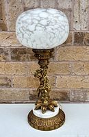 Full view of brass cherub lamp with globe shade and marble base