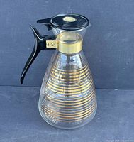 Full view showing shape, gold stripes, handle, lid