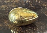 Side view of brass egg paperweight showing tarnish and shine