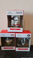 Front view of three boxed Hallmark ornaments: Snoopy, Chief Hopper, Blue Raptor