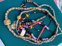 Group of four intertwined African bead necklaces showing variety of beads and brass pendant