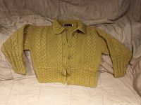 Front view of mustard wool cable-knit cardigan laid flat showing six wooden buttons