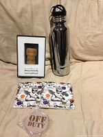 Front view of all items: chrome bottle keeper, cork shadow box, two ceramic coasters, packaged wooden opener