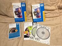 Front view of two HP Advanced Photo Paper boxes, one HP Premium Plus Photo Paper pack and two HP CD sleeves