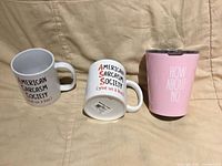 Front view of two mugs and pink tumbler showing printed text