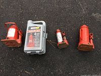 Four bottle jacks lined up on asphalt; three 4-ton, one 2-ton; one 4-ton in grey case
