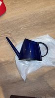 Left side view of blue plastic watering can lying on plastic bag