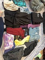Assorted folded women’s garments laid out including lace top, teal top, multiple black pieces, jeans, colourful tops and shorts