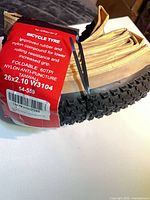 Folded tan sidewall bicycle tire with red label showing tire specs