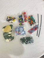 All eight sealed bags of mixed building brick pieces and two loose flexible rods displayed on white surface