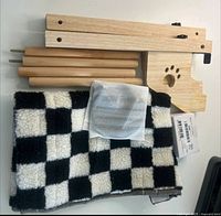 All components laid out: wood bracket with paw print cutout, four wood dowels, folded checkered fleece hammock, hardware pouch missing screws, instruction sheet