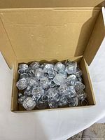 Open box showing numerous clear faceted square acrylic knobs with grey bases and washers