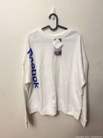 Front view of white Reebok crewneck sweatshirt showing sleeve logo and tag