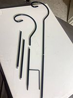 All disassembled parts: two curved hook tops, two straight extension tubes, two ground stake ends (one with foot step visible), dark powder-coated metal