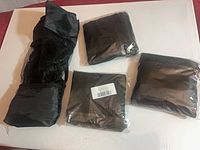Four items: three sealed black packing cubes and one rolled mesh bag displayed on surface