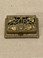 Closed brass stamp box showing sunflower motif and beaded border