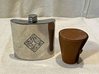 Front view of pewter flask next to closed leather case