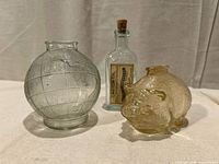 Front view of all three glass items: globe bank, pig bank, castor oil bottle