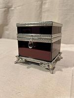 Front view of aubergine glass box with silver-tone trim and feet