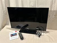 Front view of RCA 32" LED TV on stand with remote, manual, power cord