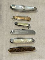 Six closed folding knives laid vertically showing handle materials and sizes