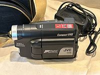 Left side view of JVC Compact VHS camcorder with 300x digital zoom label and attached AC adapter lead