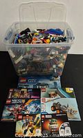 Plastic tote filled with assorted LEGO bricks with manuals laid out