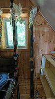 Two pairs cross-country skis standing upright, tips covered, next to shelving