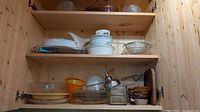 Cabinet shelves showing assorted glass, ceramic, plastic and metal kitchenware items