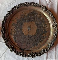 Front view of ornate round platter showing grape border and monogrammed center