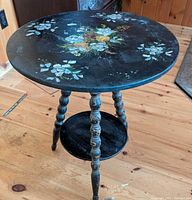 Full view of round black table showing inlay, legs, shelf, surrounding floor for scale
