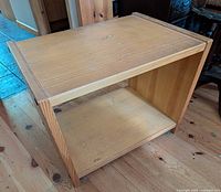 Angled view of stand showing top, one open shelf and wood grain